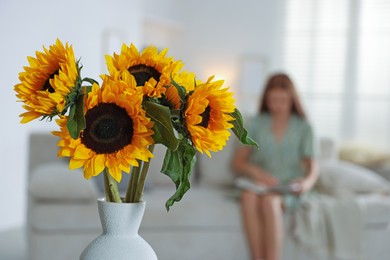 Photo of Girl reading book at home, focus on beautiful sunflowers in vase