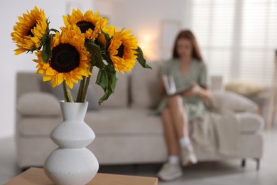Photo of Girl reading book at home, focus on beautiful sunflowers in vase