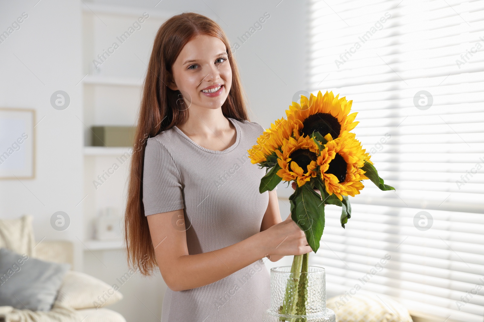 Photo of Teenage girl with beautiful sunflowers at home