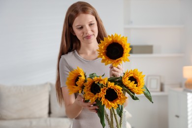 Photo of Teenage girl with beautiful sunflowers at home