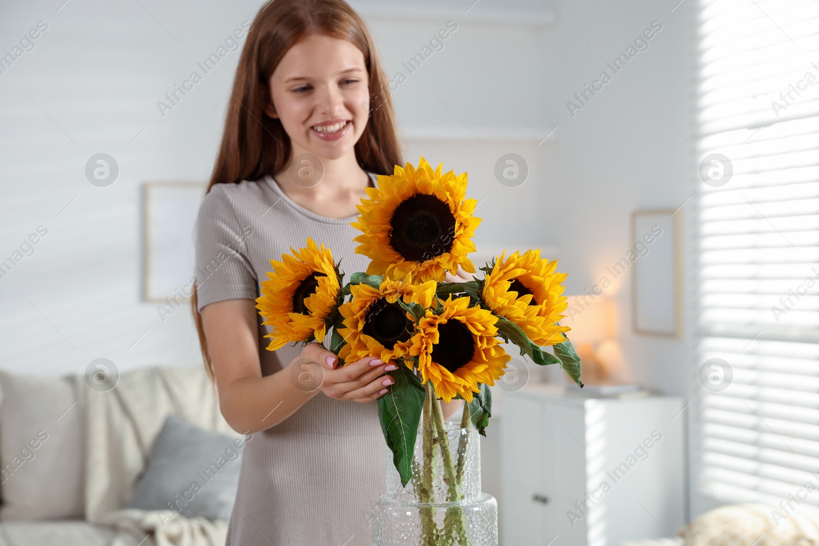 Photo of Teenage girl with beautiful sunflowers at home