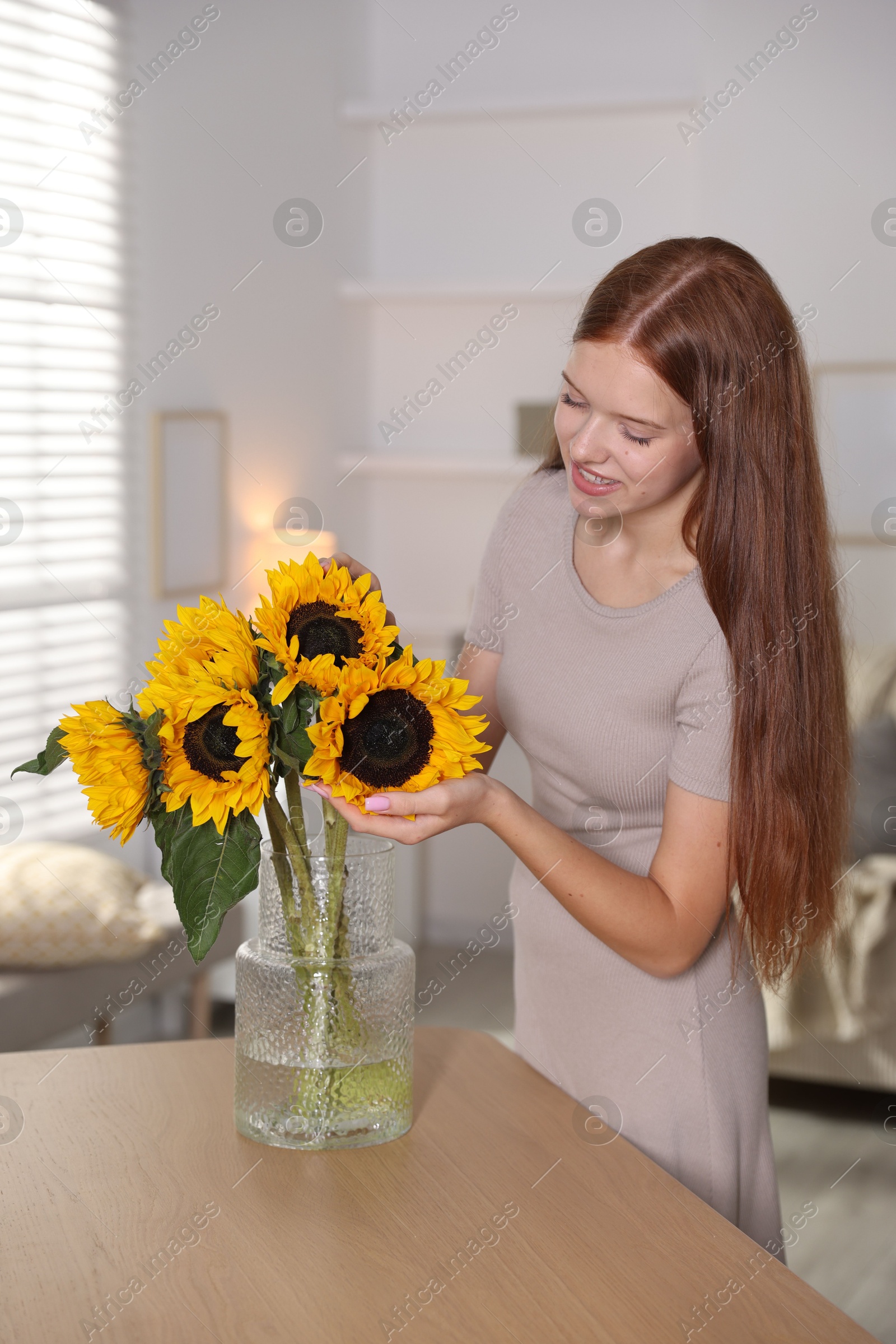 Photo of Teenage girl with beautiful sunflowers at home