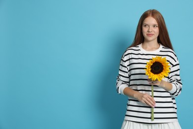 Photo of Teenage girl with sunflower on light blue background, space for text