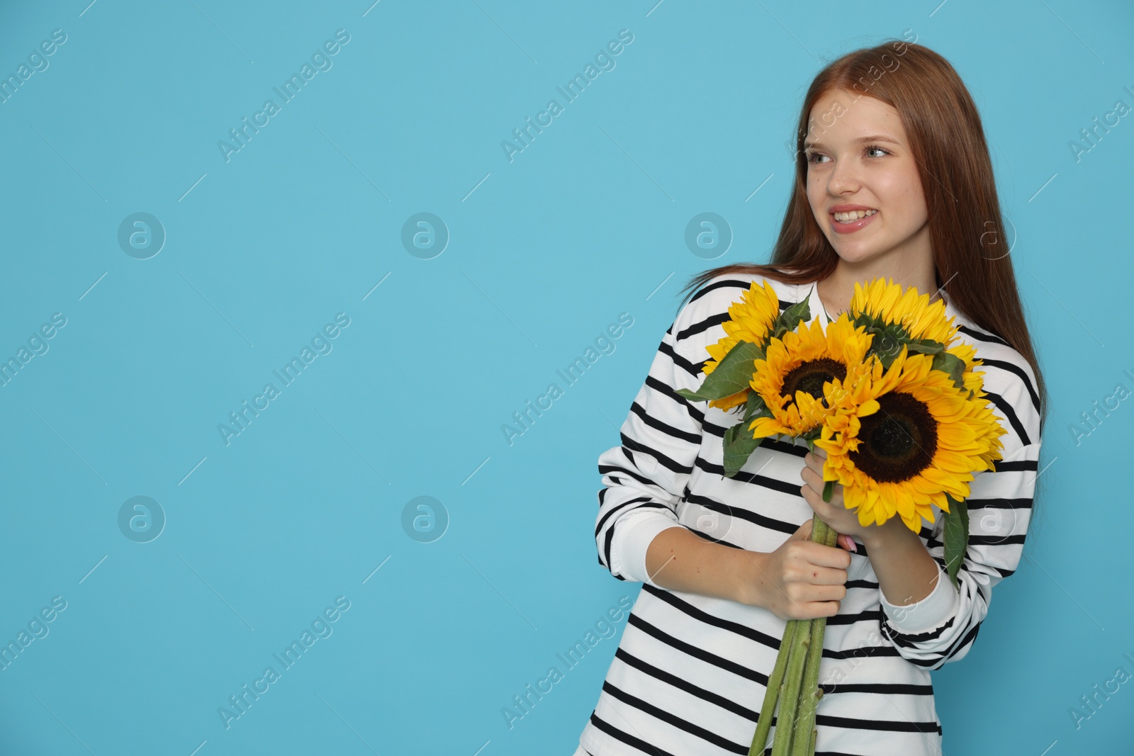 Photo of Teenage girl with bouquet of beautiful sunflowers on light blue background, space for text