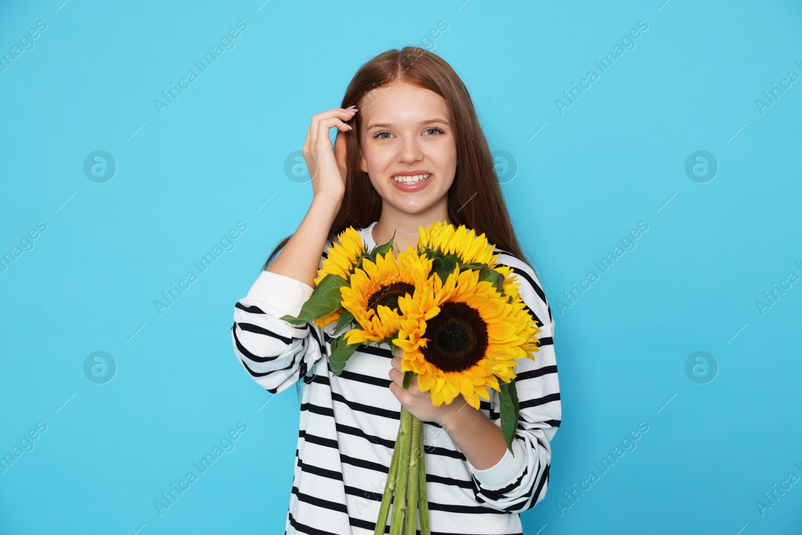 Photo of Teenage girl with bouquet of beautiful sunflowers on light blue background