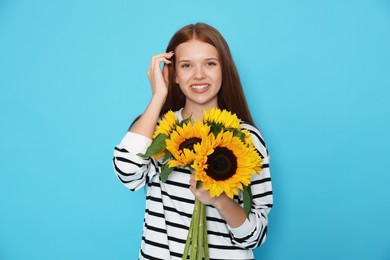 Photo of Teenage girl with bouquet of beautiful sunflowers on light blue background