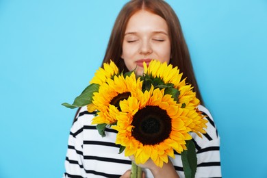 Photo of Teenage girl with bouquet of beautiful sunflowers on light blue background