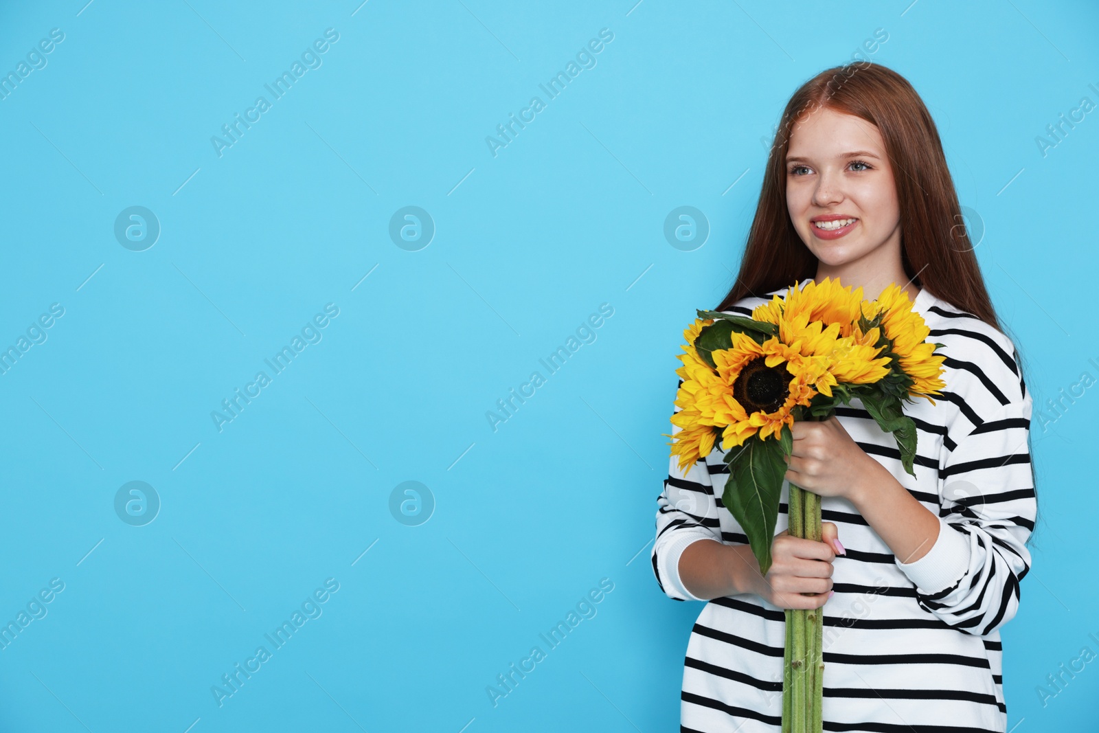 Photo of Teenage girl with bouquet of beautiful sunflowers on light blue background, space for text