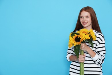Photo of Teenage girl with bouquet of beautiful sunflowers on light blue background, space for text