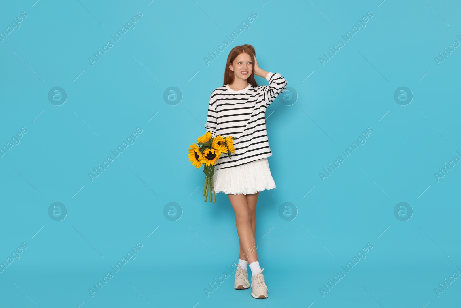 Photo of Teenage girl with bouquet of beautiful sunflowers on light blue background
