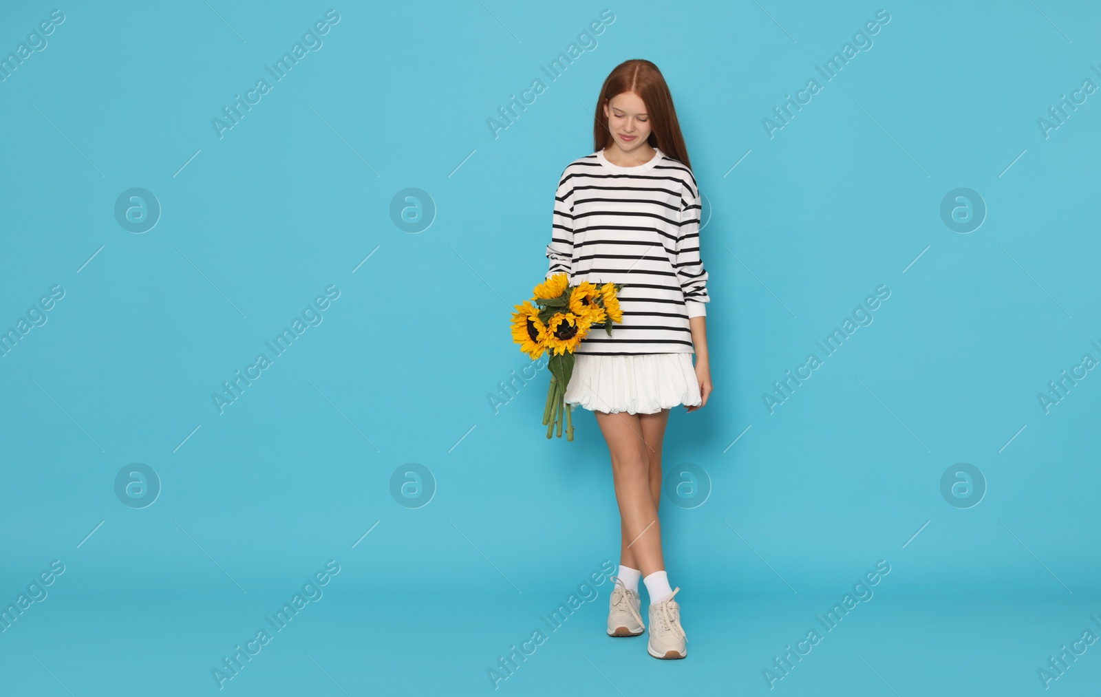 Photo of Teenage girl with bouquet of beautiful sunflowers on light blue background, space for text