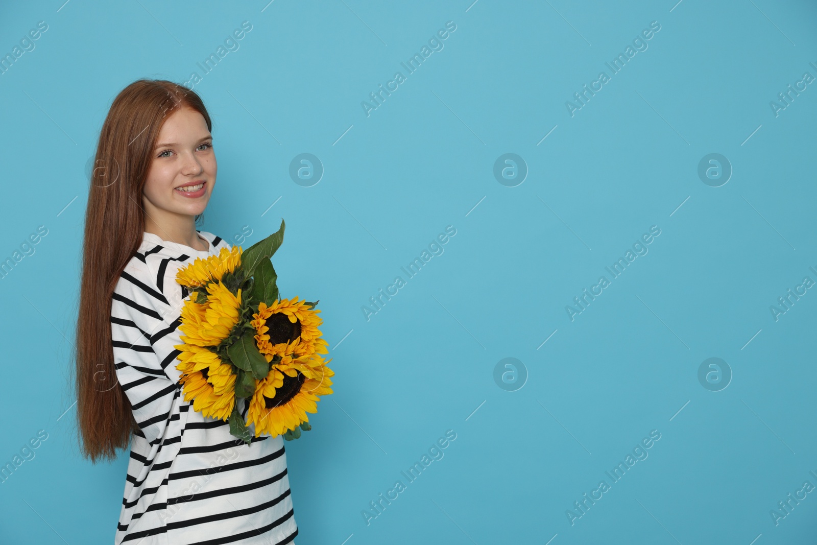 Photo of Teenage girl with bouquet of beautiful sunflowers on light blue background, space for text