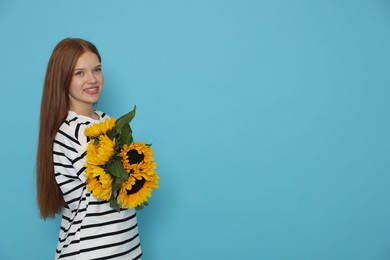 Photo of Teenage girl with bouquet of beautiful sunflowers on light blue background, space for text