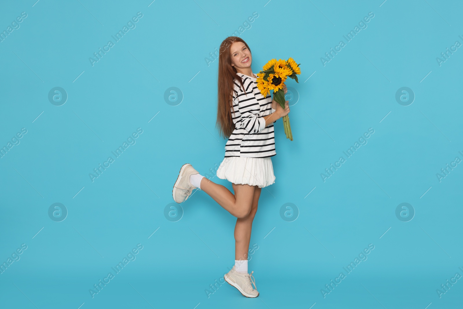 Photo of Teenage girl with bouquet of beautiful sunflowers on light blue background