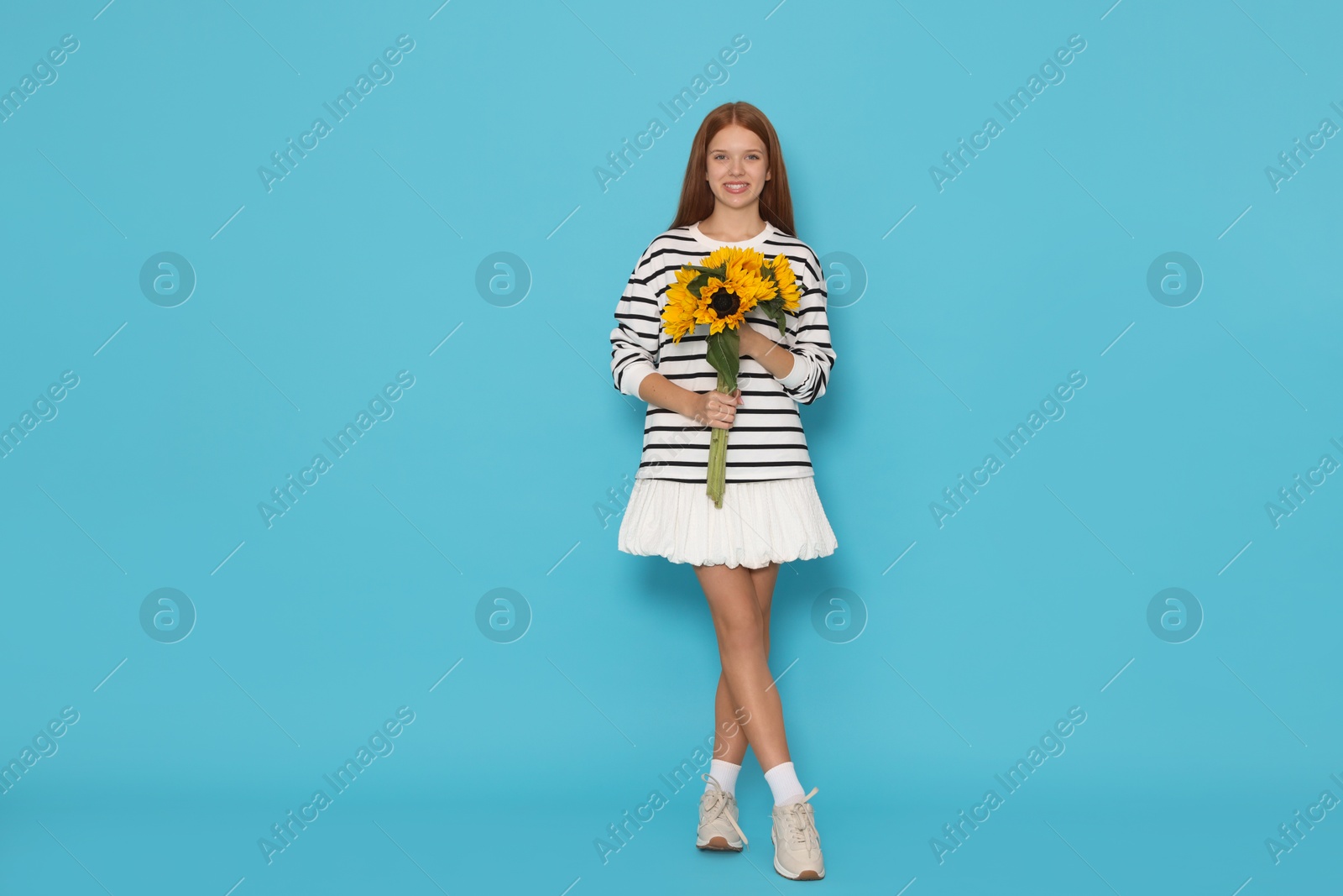 Photo of Teenage girl with bouquet of beautiful sunflowers on light blue background