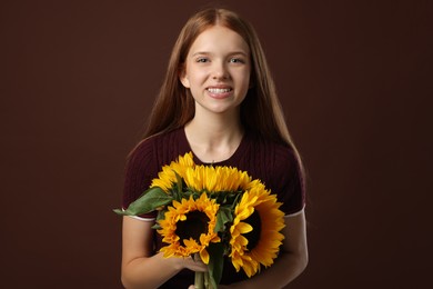 Photo of Teenage girl with bouquet of beautiful sunflowers on brown background