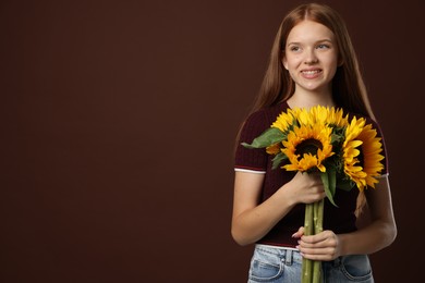 Photo of Teenage girl with bouquet of beautiful sunflowers on brown background, space for text