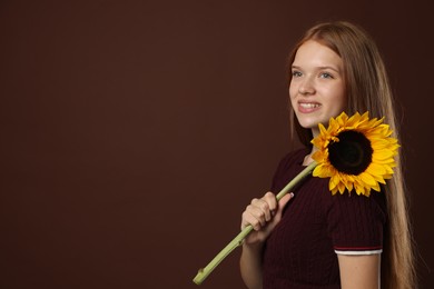 Photo of Teenage girl with beautiful sunflower on brown background, space for text
