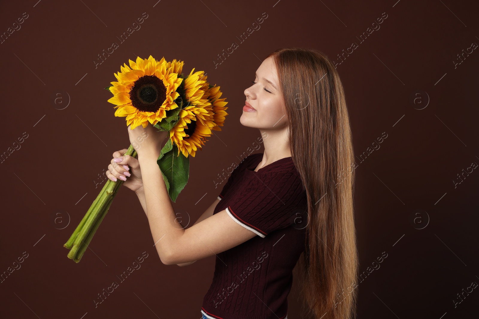 Photo of Teenage girl with bouquet of beautiful sunflowers on brown background