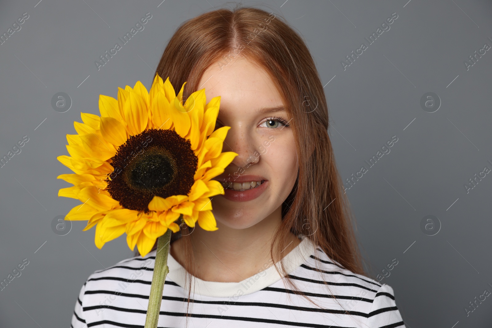Photo of Teenage girl with beautiful sunflower on grey background