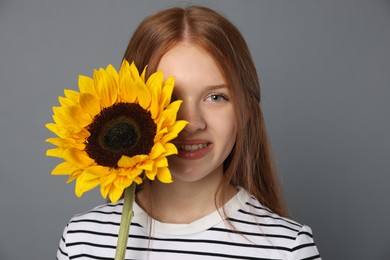Photo of Teenage girl with beautiful sunflower on grey background