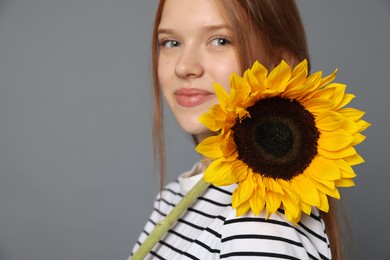 Photo of Teenage girl with beautiful sunflower on grey background, space for text