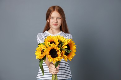 Photo of Teenage girl with bouquet of beautiful sunflowers on grey background, selective focus