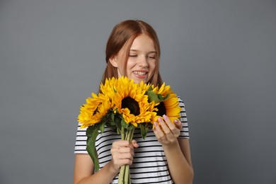 Photo of Teenage girl with bouquet of beautiful sunflowers on grey background