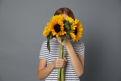Photo of Teenage girl with bouquet of beautiful sunflowers on grey background