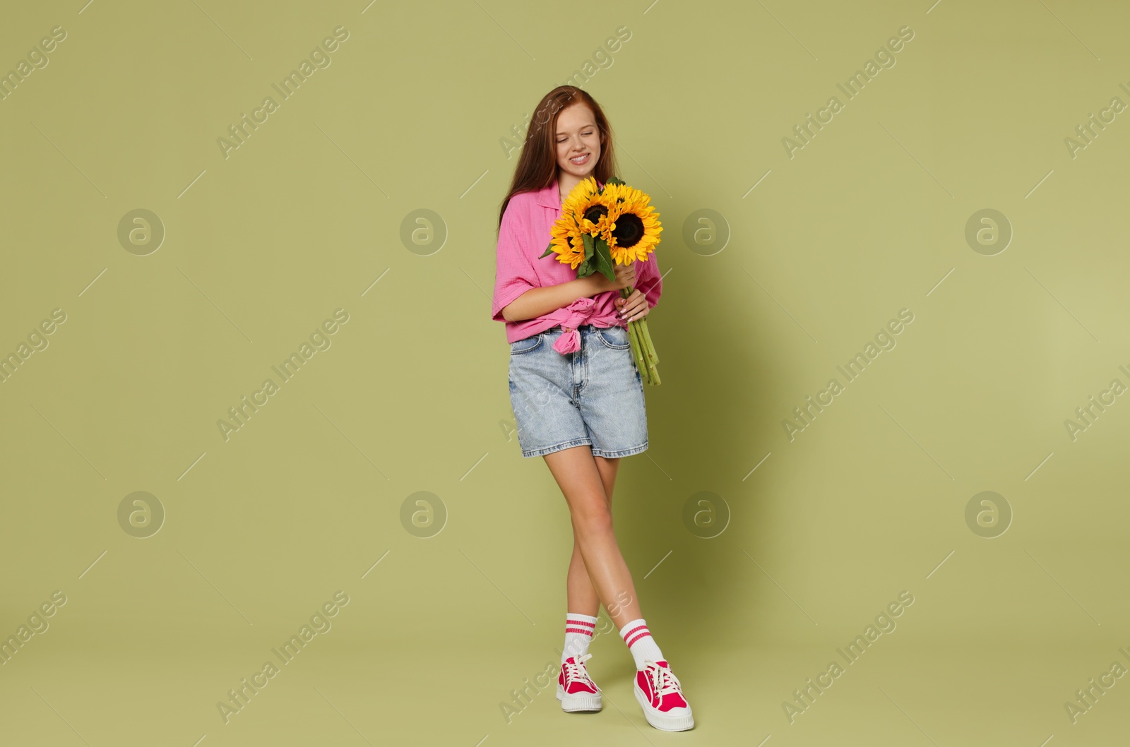 Photo of Teenage girl with bouquet of beautiful sunflowers on green background