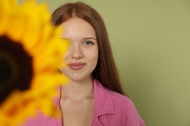 Photo of Teenage girl with beautiful sunflower on green background, selective focus. Space for text