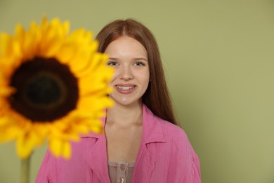 Photo of Teenage girl with beautiful sunflower on green background, selective focus