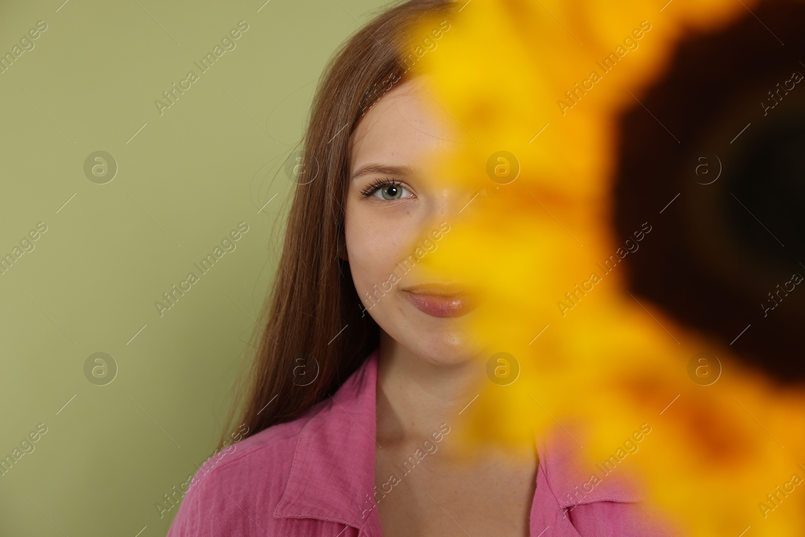 Photo of Teenage girl with beautiful sunflower on green background, selective focus
