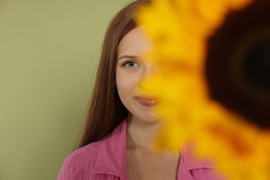 Photo of Teenage girl with beautiful sunflower on green background, selective focus