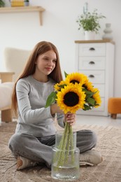 Photo of Teenage girl putting beautiful sunflowers into vase at home
