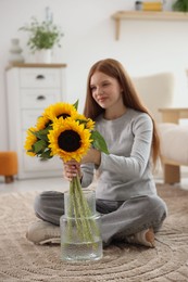 Photo of Teenage girl putting beautiful sunflowers into vase at home