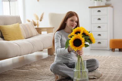 Photo of Teenage girl putting beautiful sunflowers into vase at home