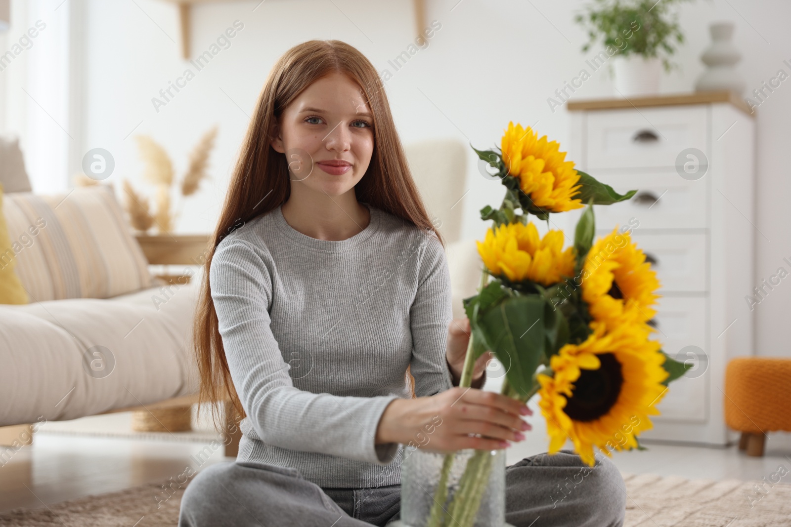 Photo of Teenage girl putting beautiful sunflowers into vase at home