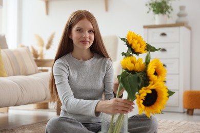Photo of Teenage girl putting beautiful sunflowers into vase at home