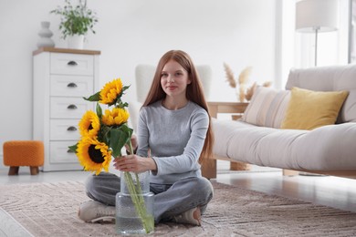 Photo of Teenage girl putting beautiful sunflowers into vase at home