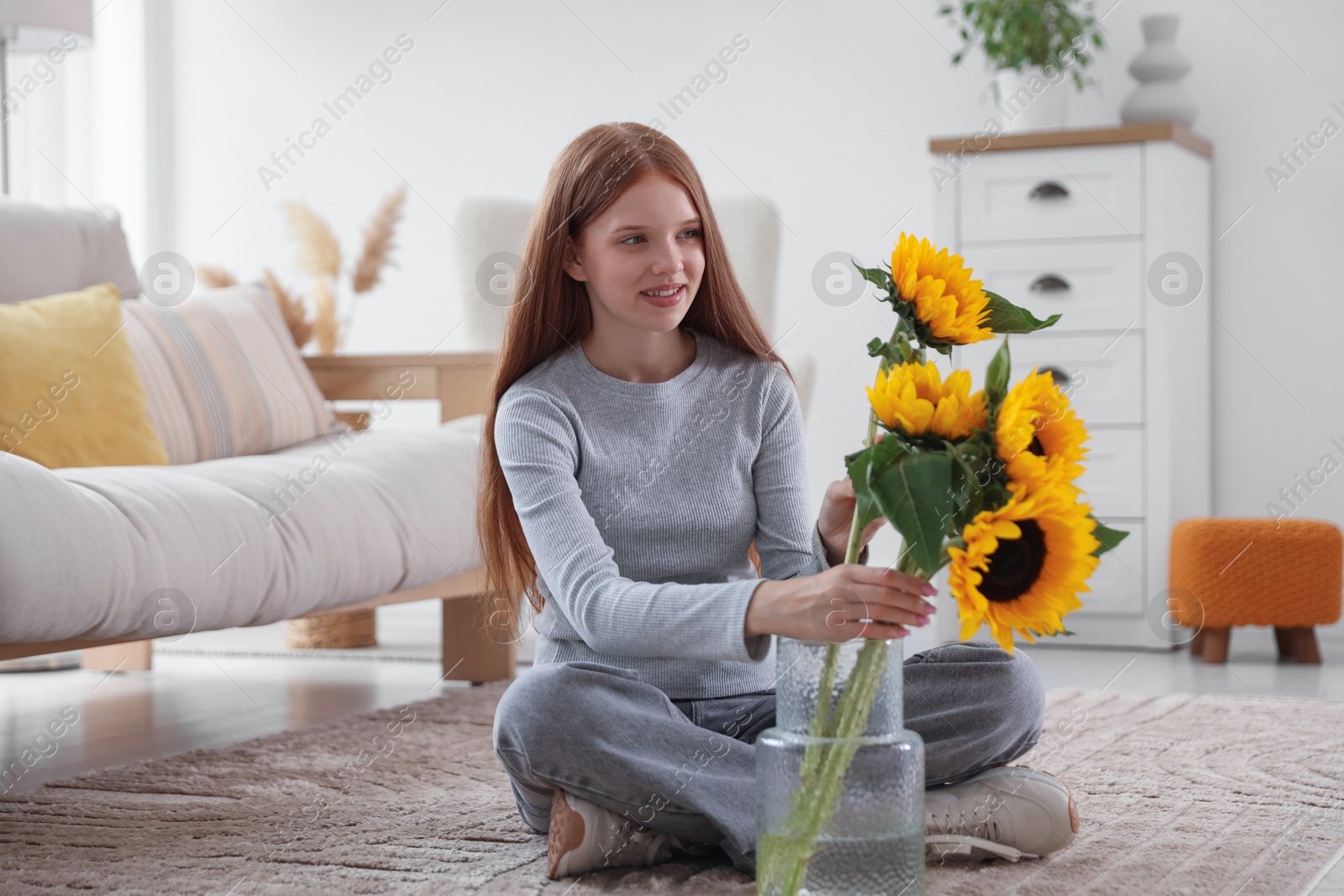 Photo of Teenage girl putting beautiful sunflowers into vase at home