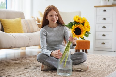 Photo of Teenage girl putting beautiful sunflowers into vase at home