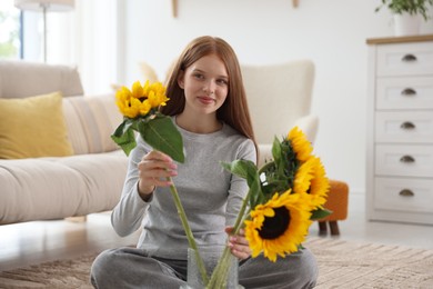 Photo of Teenage girl putting beautiful sunflowers into vase at home