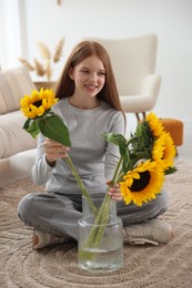 Photo of Teenage girl putting beautiful sunflowers into vase at home