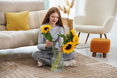 Photo of Teenage girl putting beautiful sunflowers into vase at home