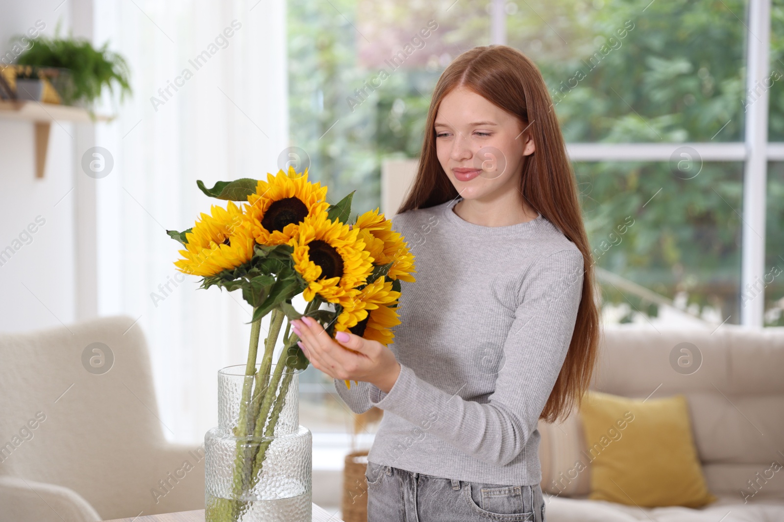 Photo of Teenage girl with beautiful sunflowers at home