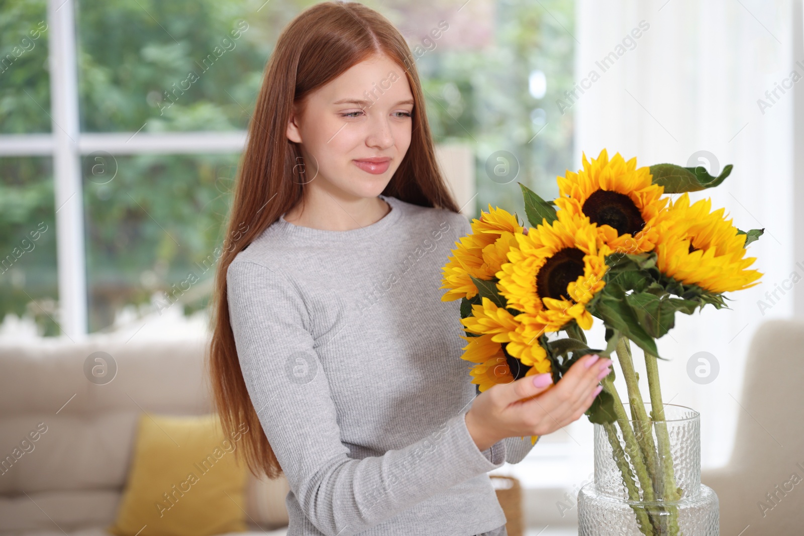 Photo of Teenage girl with beautiful sunflowers at home
