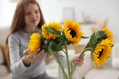 Photo of Teenage girl with beautiful sunflowers at home, selective focus