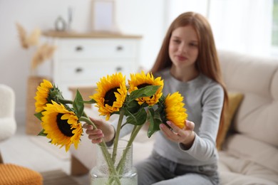 Photo of Teenage girl with beautiful sunflowers at home, selective focus
