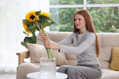 Photo of Teenage girl putting beautiful sunflowers into vase at home